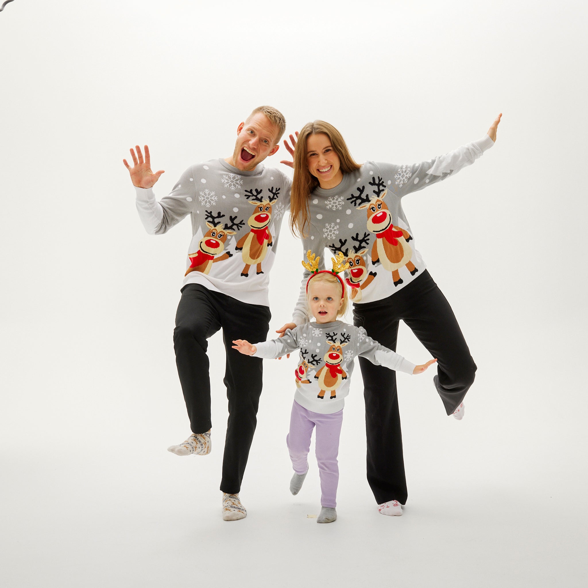 Familie trägt graue Weihnachtspullover mit Rentier- und Schneemann-Motiv, lächelnd und fröhlich poseierend.