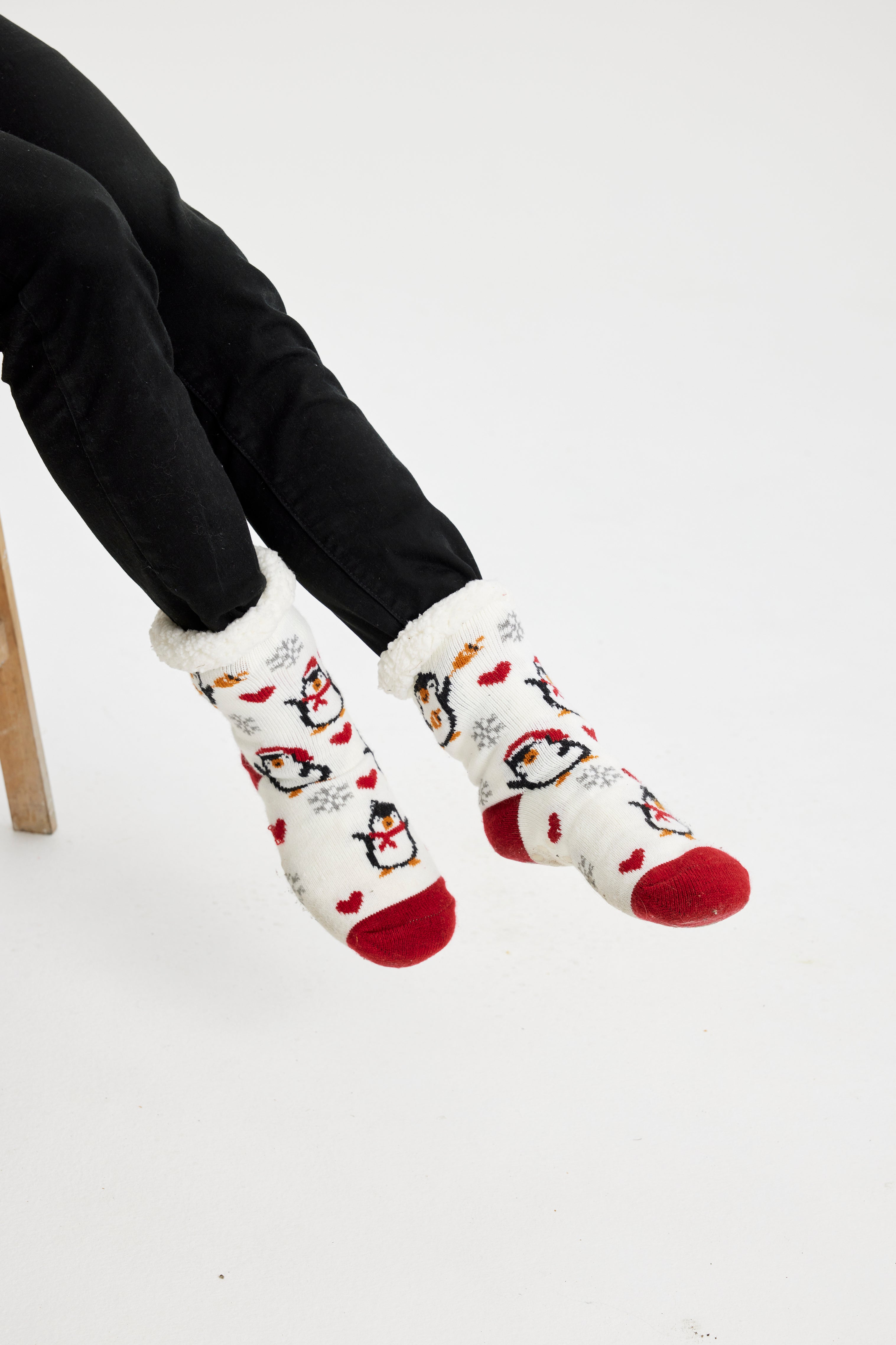 Ein Paar Beine, die ein Paar rote und weiße Weihnachtssocken mit Pinguinen darauf tragen.