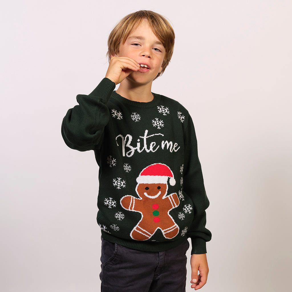 Ein Kind in einem grünen Weihnachtspulli mit einem Keks und Schneeflocken darauf.