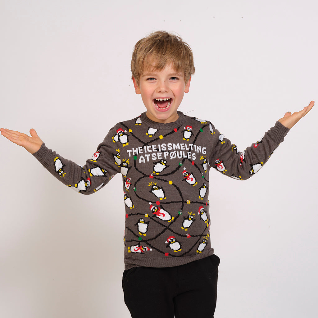 Ein Kind trägt einen braunen Weihnachtspulli mit Pinguinen und Lichtern.