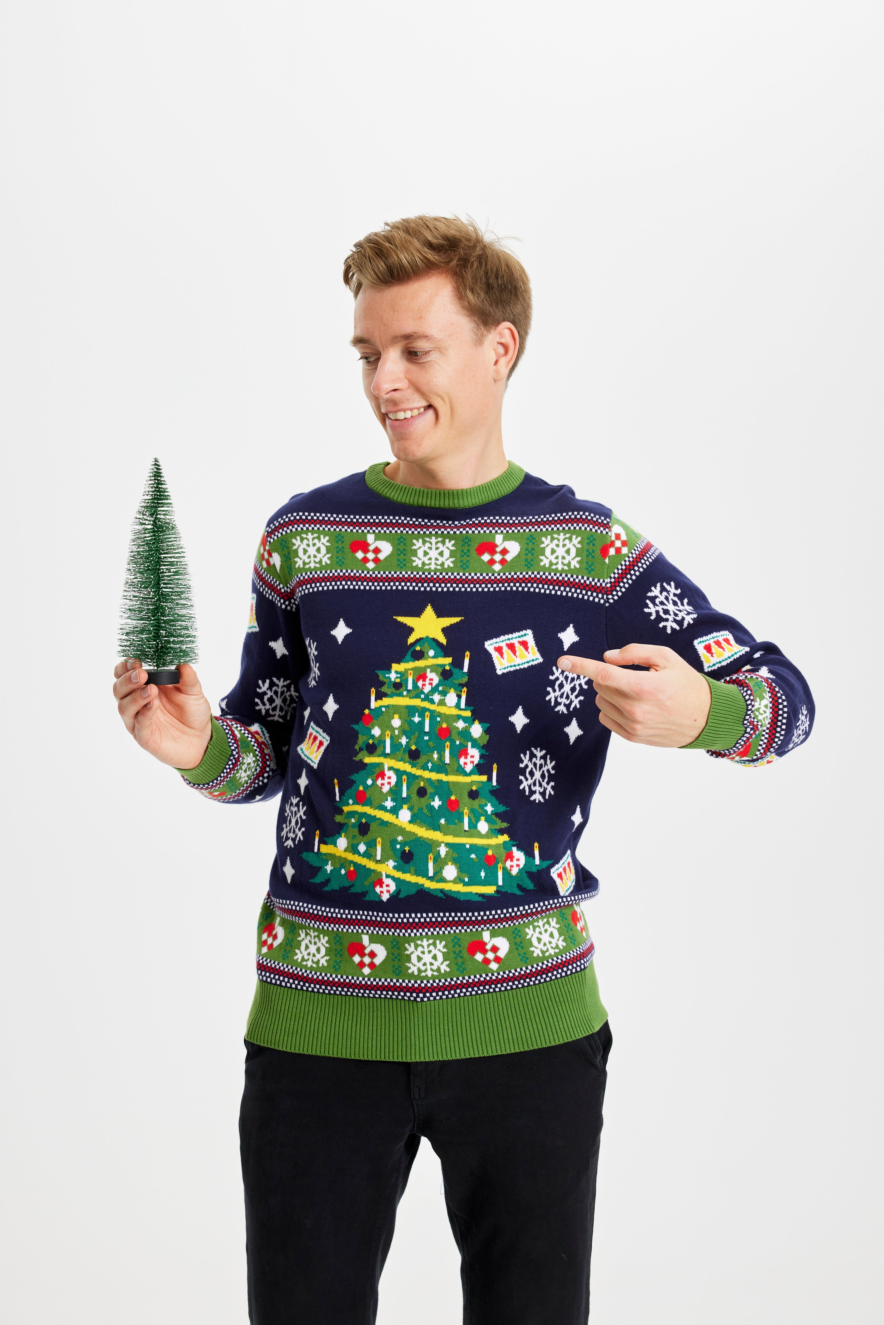 Ein Mann posiert in einem blauen und grünen Weihnachtspullover mit einem Weihnachtsbaum.