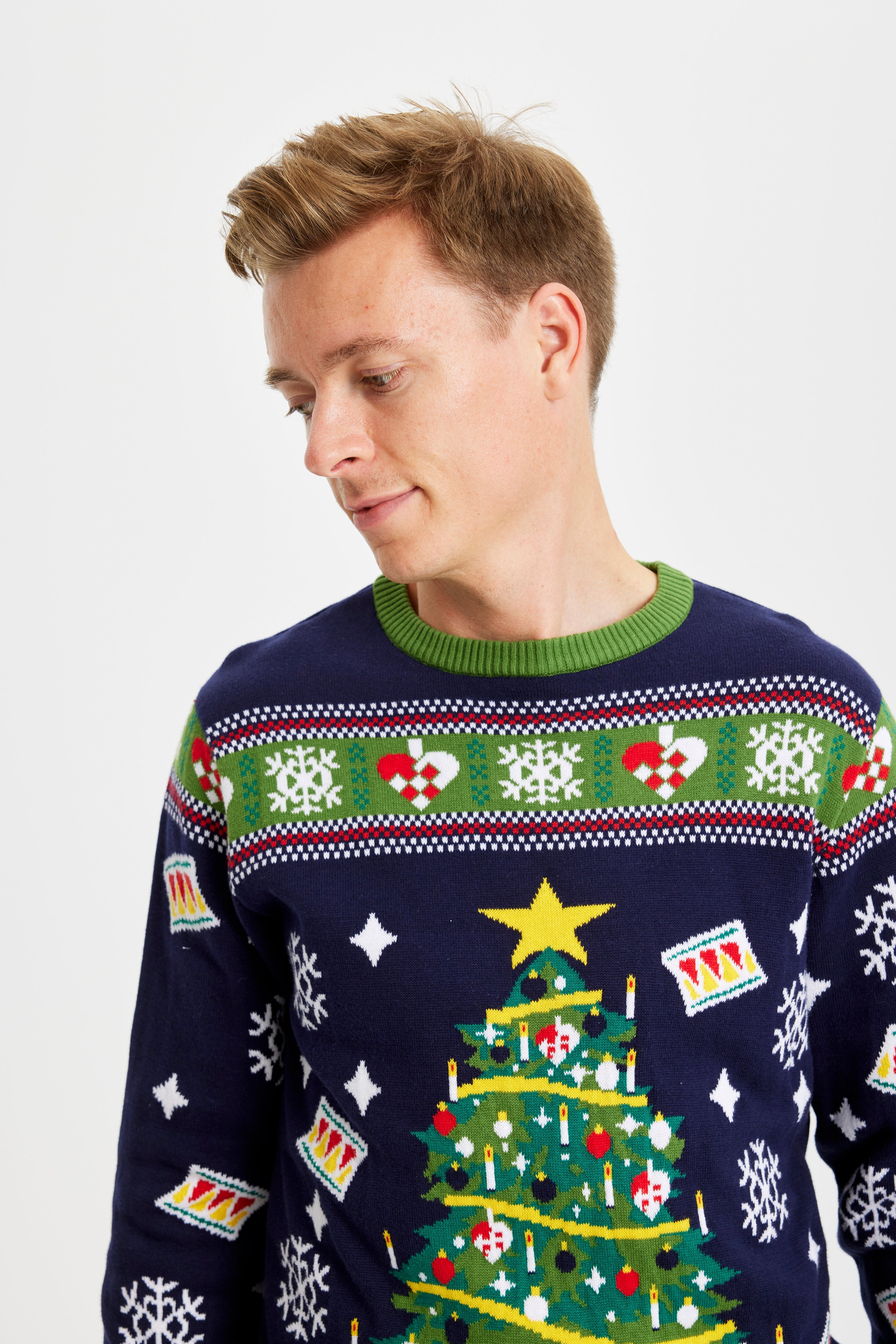 Ein Mann in einem blau-grünen Weihnachtspulli mit Weihnachtsbaum schaut zur Seite.