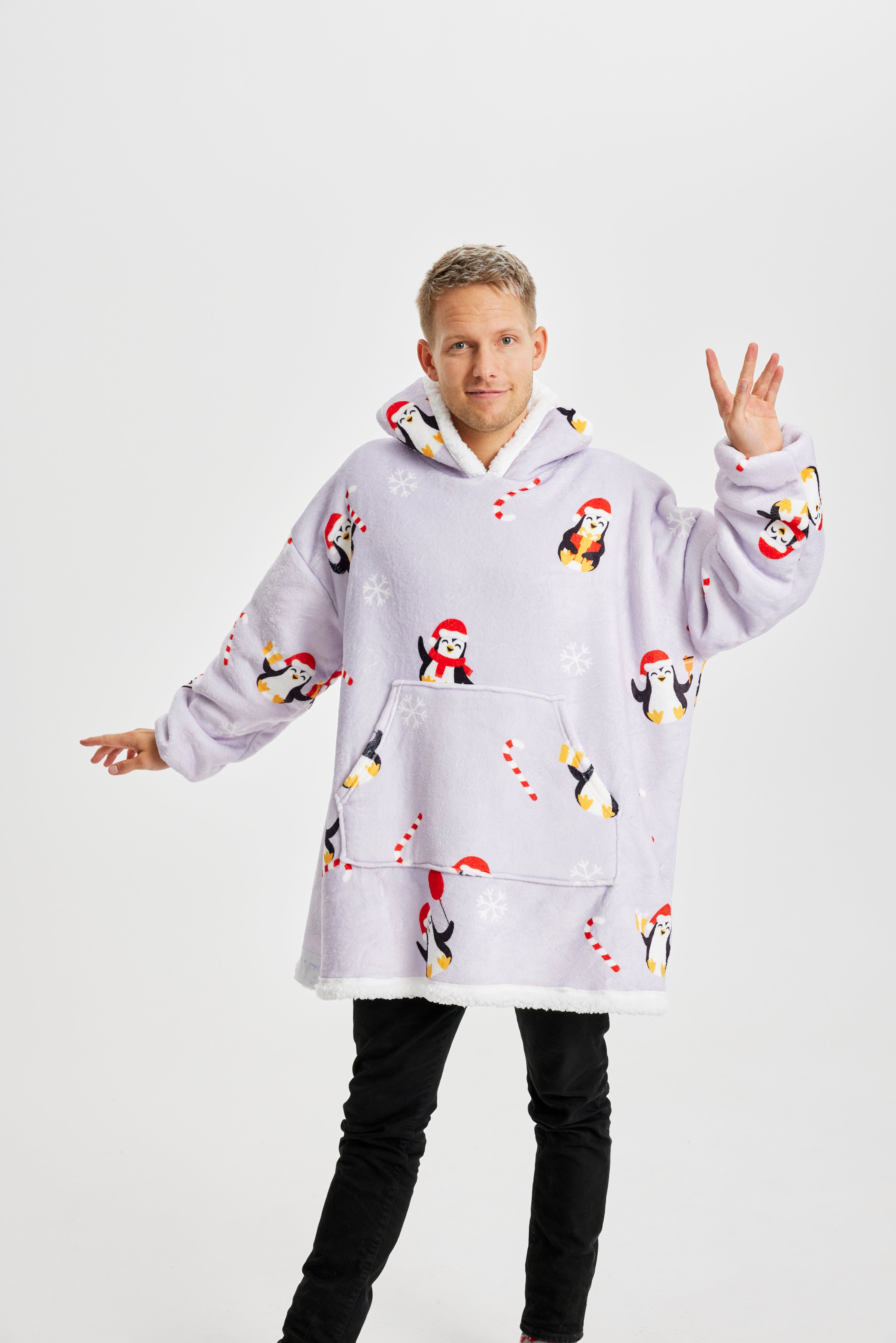 Ein Mann mit den Händen in der Luft, der einen helllila Weihnachtskapuzenpullover mit Pinguinen darauf trägt.