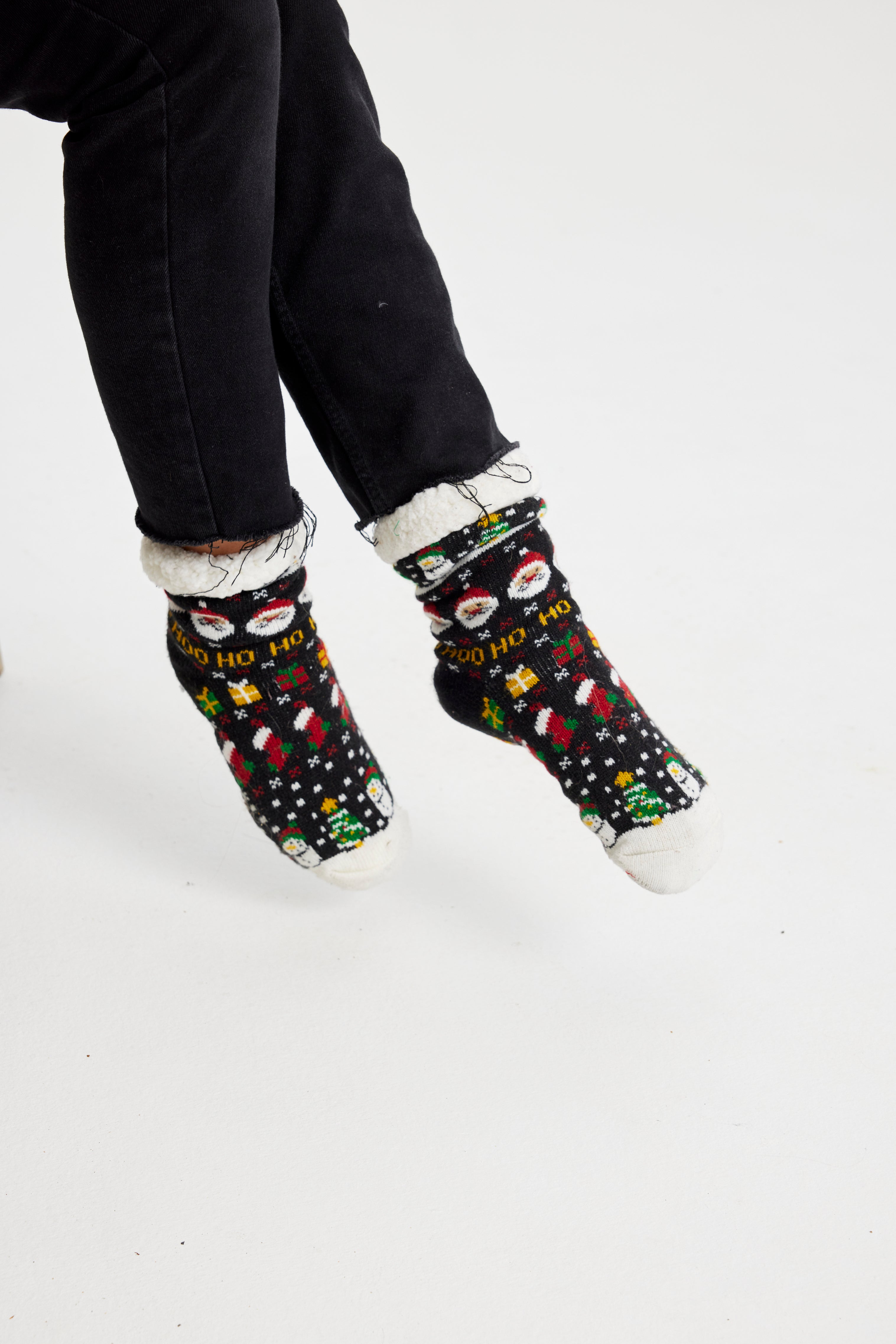 Ein Paar Beine, die ein Paar schwarze Weihnachtssocken mit einem Weihnachtsmuster darauf tragen.