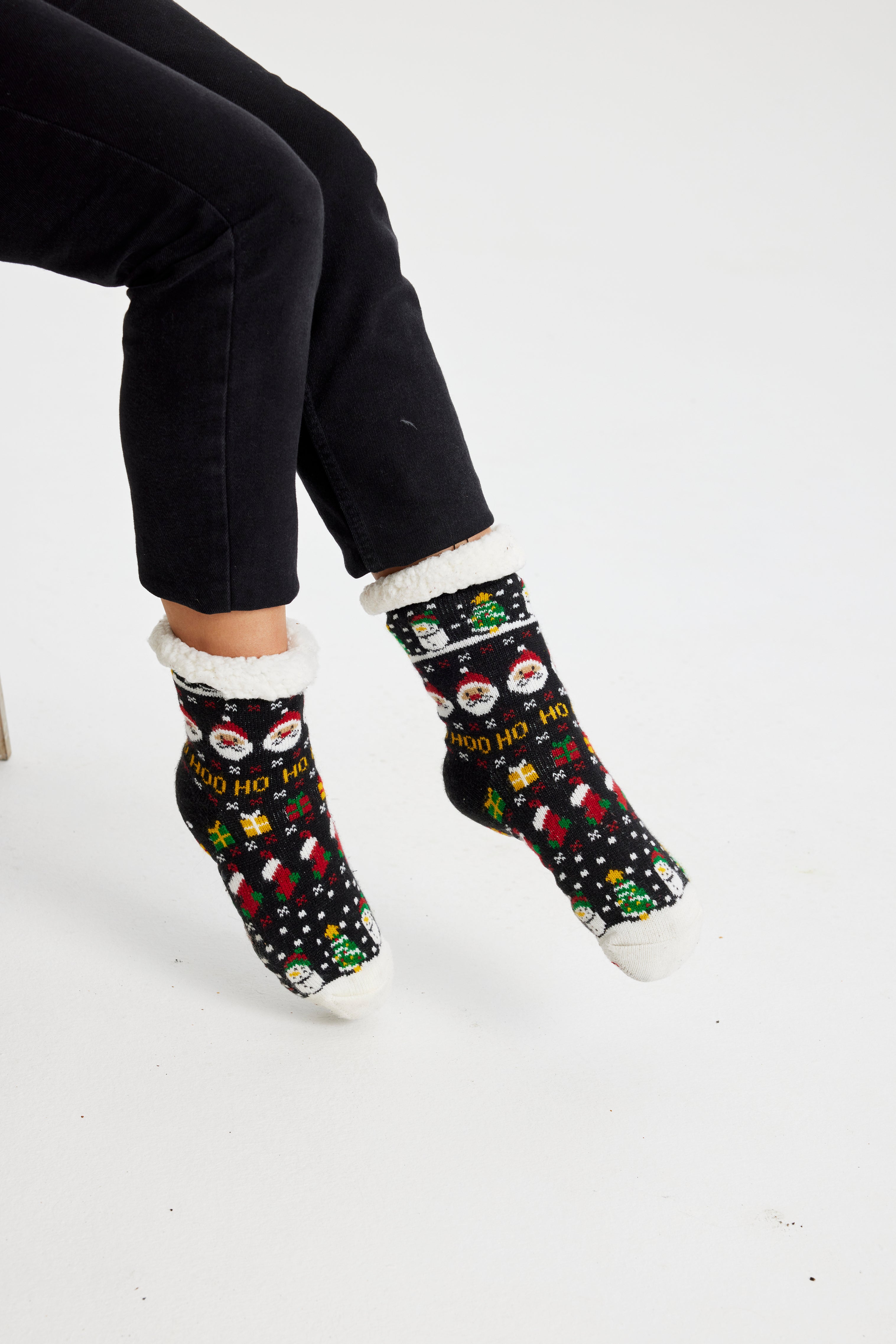 Ein Paar Beine, die ein Paar schwarze Weihnachtssocken mit einem Weihnachtsmuster darauf tragen.