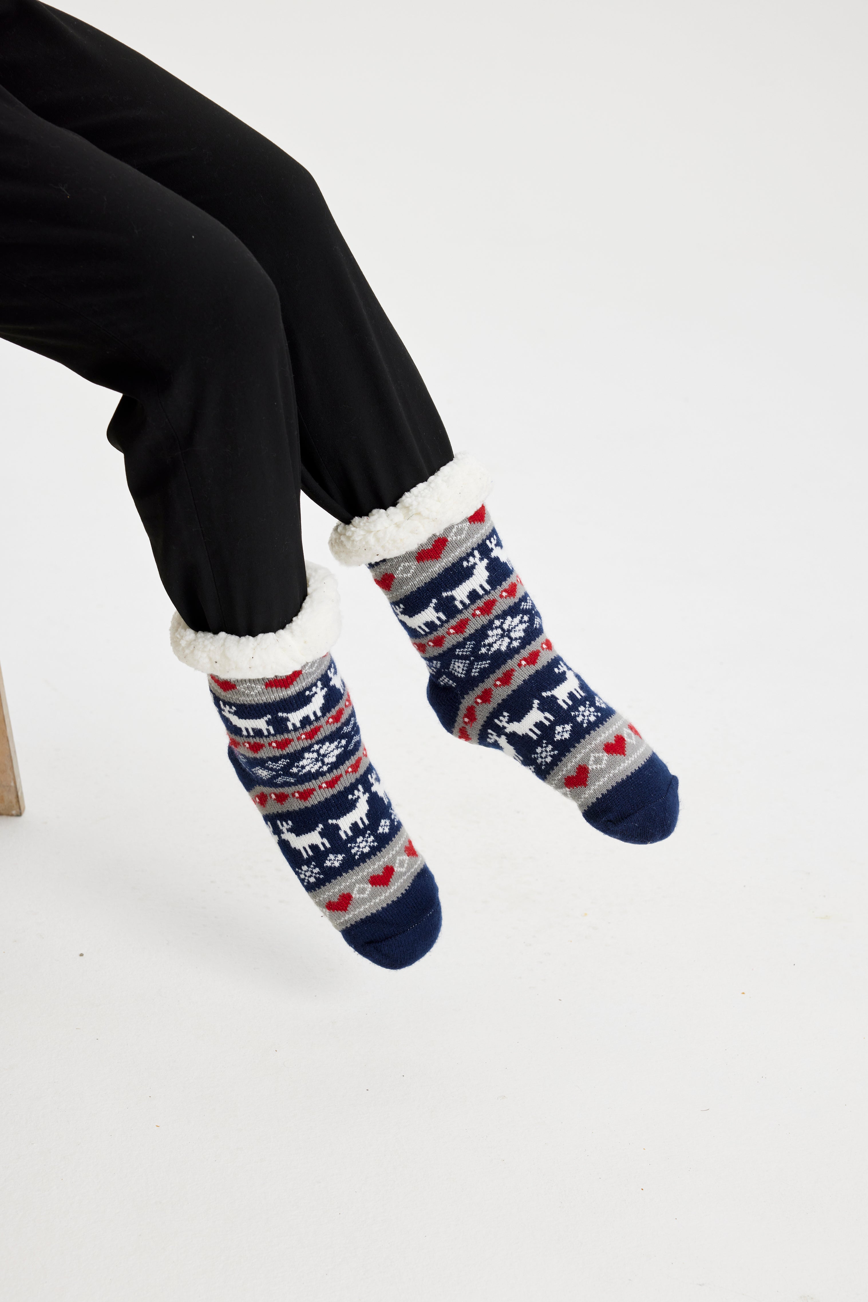 Ein Paar Beine, die ein Paar blaue und weiße Weihnachtssocken mit einem Weihnachtsmuster tragen.