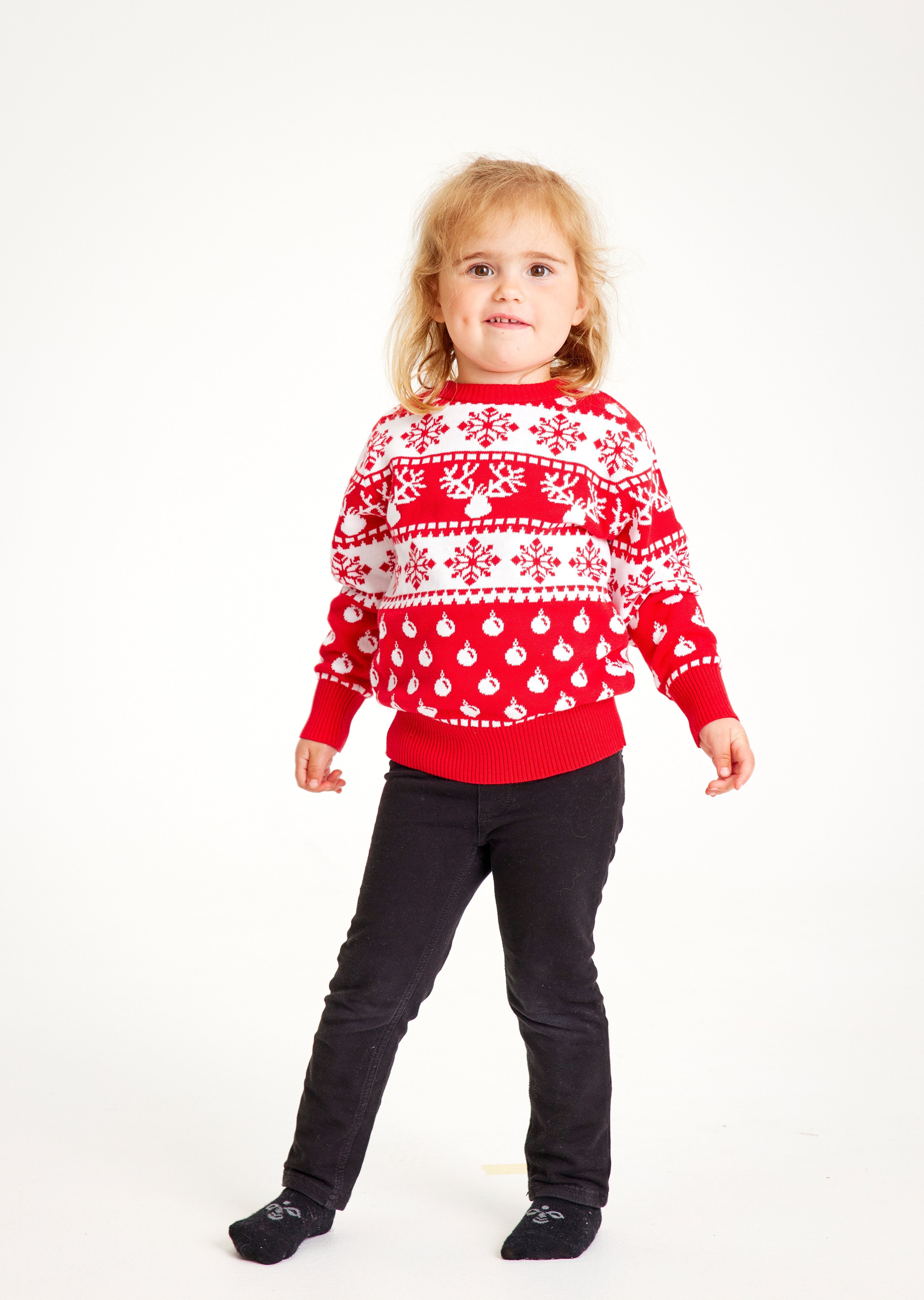 Ein Kind posiert in einem rot-weißen Weihnachtspulli mit Schneeflocken.